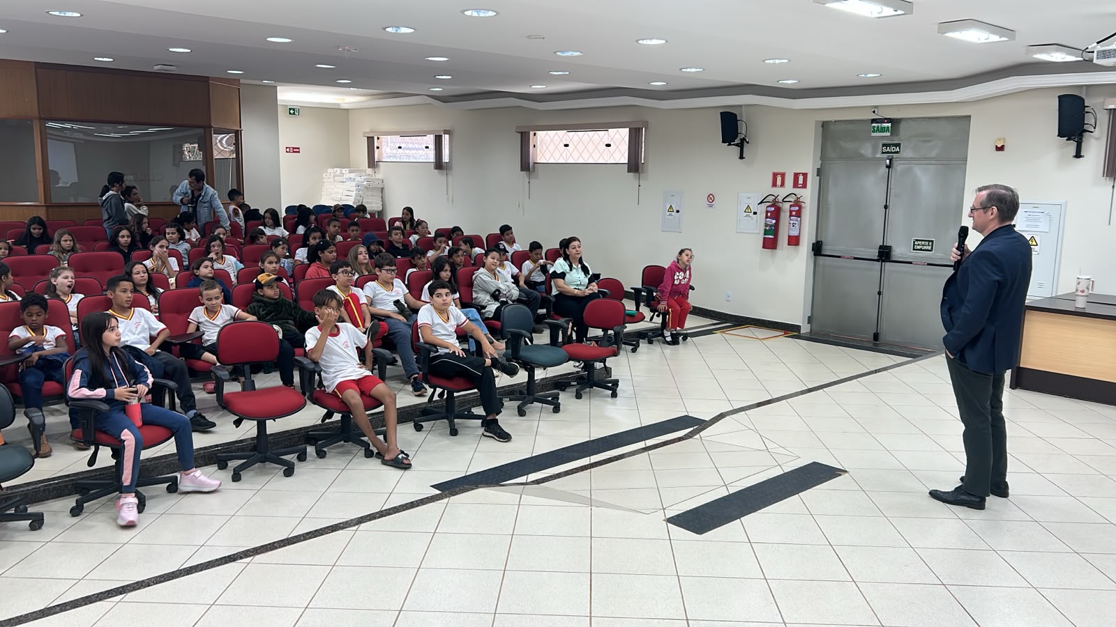 Fotografia mostra promotor falando para alunos no auditório